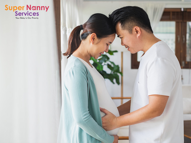 Husband placing his palms on his wife's belly as a form of support for his wife with their foreheads touching