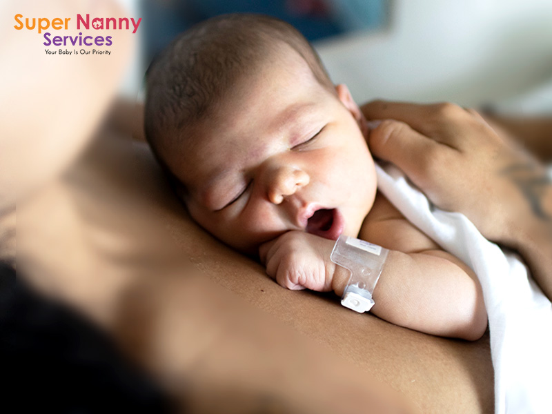 Newborn baby wrapped in white blanket resting on mother’s chest with hospital ID band visible.